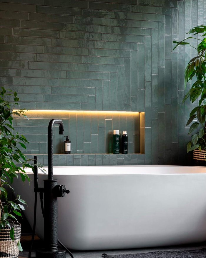 Badkamer met groene handvormtegels, een vrijstaand bad en een verlichte nis